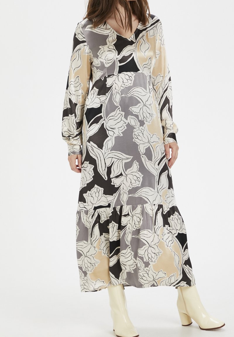 Lång, flödande klänning med ett blommönster i beige, grå och svarta nyanser. V-ringning, långa ärmar och en lager-på-lager kjol i mjukt tyg.