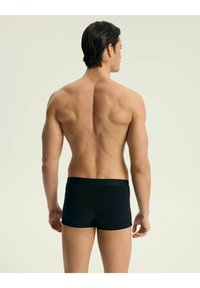 Czarne bokserki o gładkiej fakturze, z szerokim elastycznym paskiem w talii. Plecy modela są odwrócone, co eksponuje krój i fason.
