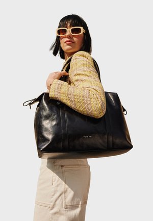 Bolso tote de cuero negro con herrajes plateados, que presenta una textura lisa, dos costuras laterales y un logotipo grabado cerca de la base.