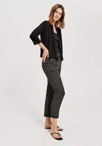 Zwarte open voorkaart met ¾ mouwen, gecombineerd met geblokte zwart-witte cropped broek. Gemaakt met zwarte platte sandalen.