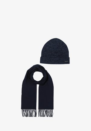Cappello a maglia color blu navy scuro con una texture a coste e risvolto piegato, abbinato a una sciarpa lunga coordinata con estremità frange.