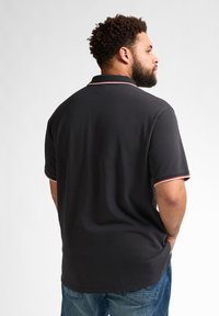 Czarna koszulka polo z kołnierzykiem i czerwono-białymi akcentami na rękawach, w połączeniu z niebieskimi dżinsami. Gładka tkanina i luźny krój.