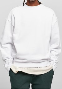 Vit oversized sweatshirt med sänkta axlar, ribbat nacke och texturerad nederkant. Kombination med gröna texturerade byxor och ljus underlayer.