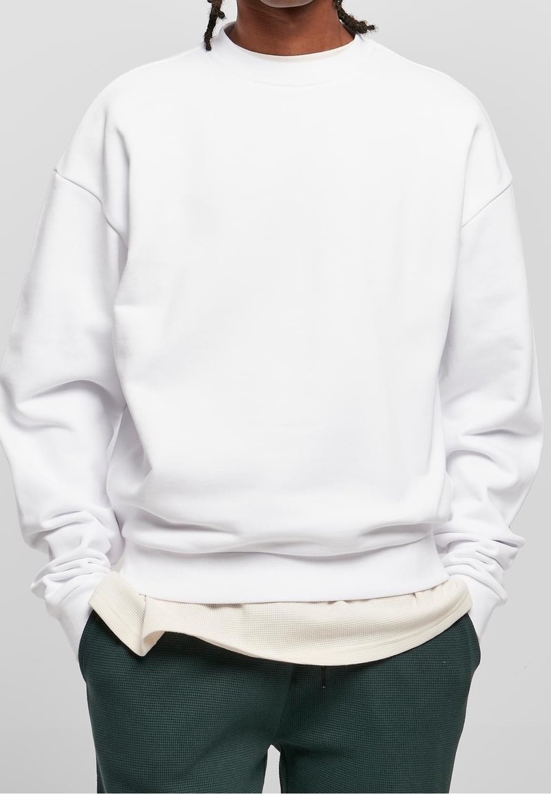 Vit oversized sweatshirt med sänkta axlar, ribbat nacke och texturerad nederkant. Kombination med gröna texturerade byxor och ljus underlayer.