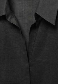 Sort linned shirt med spids krave, glat tekstur og subtil glans. Stoffet fremstår let og har en afslappet pasform.