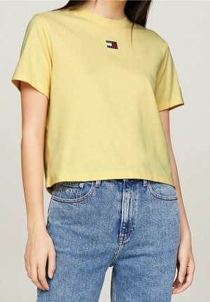 Geel katoenen t-shirt met korte mouwen, ronde halslijn en een cropped ontwerp. Beschikt over een kleine logo patch in rood, wit en blauw.