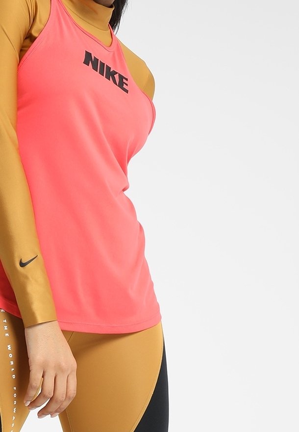 Nike pink ärmelloses Top mit schwarzem Logo, kombiniert mit einem goldenen Langarm-Basisschicht und schwarzen Leggings mit einem geschwungenen Farbblockdesign.