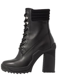 Botín negro de cuero con parte superior texturizada, cierre de cordones gruesos y tacón angular. Presenta suela de goma con detalles antideslizantes.