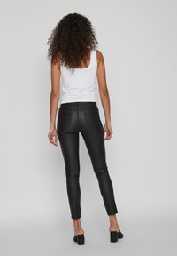 Leggings ajustados de imitación de cuero negro con una textura suave, cintura a media altura y dos bolsillos traseros. Combinados con una simple camiseta sin mangas blanca.