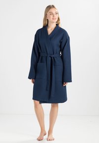 Peignoir en waffle de couleur bleu marine avec des manches longues, une fermeture par ceinture et deux poches avant, conçu pour le confort et la praticité.