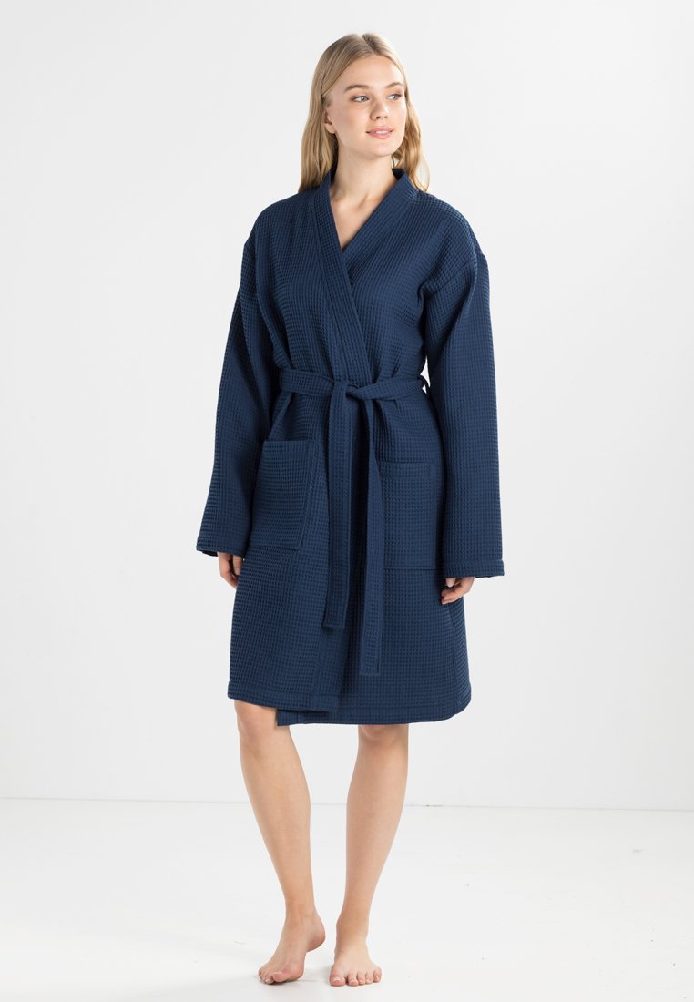 Peignoir en waffle de couleur bleu marine avec des manches longues, une fermeture par ceinture et deux poches avant, conçu pour le confort et la praticité.