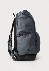 Zaino grigio con un design curvo, realizzato in tessuto resistente. Dotato di spallacci imbottiti, chiusura con cerniera e molteplici tasche per riporre gli oggetti.