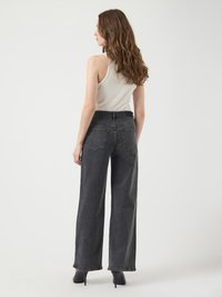 Jeans anchos negros con cintura alta, que cuentan con bolsillos traseros y un acabado limpio. Combinados con una blusa sin mangas color beige y tacones negros.