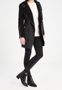 Musta mokkanahkatakki, jossa on karvareunainen kaulus, sivuvetoketjut ja epäsymmetrinen etuosa. Päällä vaalea paita, mustat kapealahkeiset farkut ja nilkkurit.