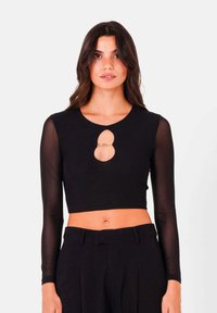 Top corto nero con maniche lunghe trasparenti, colletto rotondo e dettaglio tagliato sulla parte anteriore con un accento di catena decorativa.