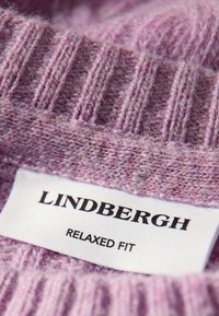 Lila stickad tröja med ribbad textur, försedd med en etikett som säger "LINDBERGH RELAXED FIT." Mjukt tyg med en avslappnad look.