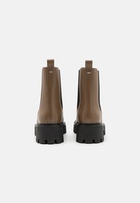 Bruine leren enkelboots met zwarte rubberen zolen, elastische zijpanelen en aantrek lipjes, met een chunky ontwerp en een getextureerde afwerking.