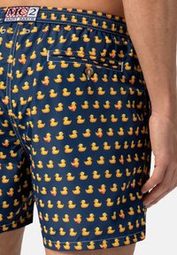 Costume da bagno in tessuto blu navy con motivo di anatre di gomma gialle. Vita elastica, tasca laterale e dettaglio di chiusura con bottone.