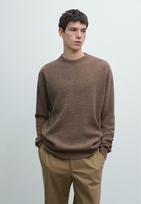 Brązowy sweter z dzianiny z okrągłym dekoltem, długimi r�ękawami i luźnym krojem, zestawiony z beżowymi spodniami. Miękka faktura, prążkowany wzór.