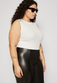 White sleeveless top made of cotton, paired with high-waisted black pants featuring a glossy leather-like material and textured details.