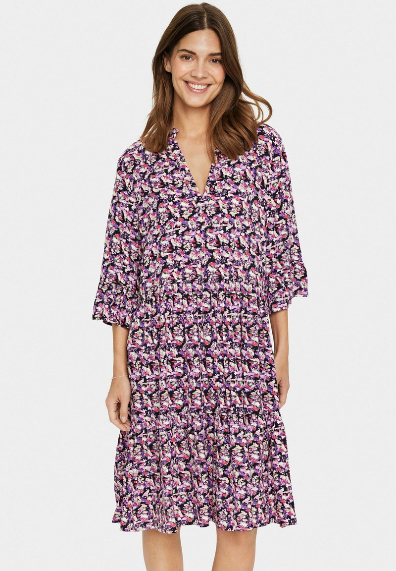 Rochie florală cu un fundal violet, având flori roz și albe, cu decolteu în V și mâneci trei sferturi. Design ușor, în straturi.
