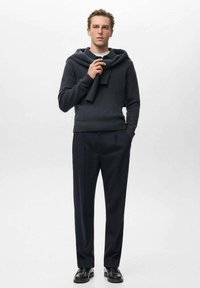Pulover gri închis cu glugă, așezat pe umeri, asortat cu pantaloni închiși la culoare și pantofi negri. Textură netedă și design ajustat.