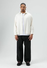 Wit overhemd over een wit T-shirt, gecombineerd met losse zwarte jeans en stevige zwarte schoenen met roze veters. Eenvoudig ontwerp, zonder print.