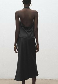 Čierna saténová top s nízkym chrbtom, v kombinácii s dlhou sukňou z rovnakého materiálu. Má voľný strih a hladkú textúru, doplnená zlatými šperkami.