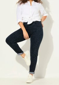 Mörkblå jeans med ett subtilt bladmönster, hög midja, uppvikt fåll, i kombination med vita sneakers och en knuten vit skjorta.