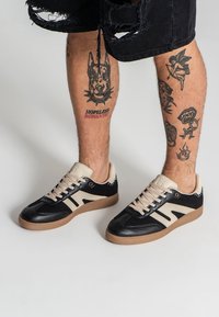 Scarpe sportive nere e beige con tomaia in pelle sintetica, dettagli decorativi, punta tonda e suola in gomma color beige chiaro.
