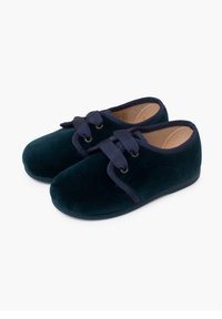 Scarpe in velluto verde scuro con punta rotonda, laccate con un nastro blu navy e dotate di una morbida fodera interna. La suola è piatta e in gomma.