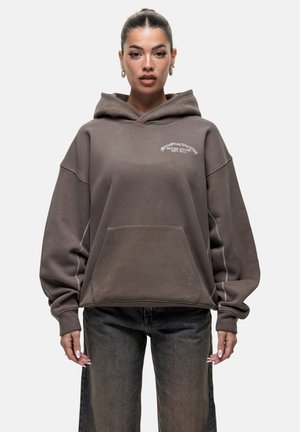 Brown oversized hoodie with a front pocket, ribbed cuffs, and embroidered logo in white. Soft fabric, casual design, and relaxed fit.