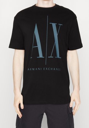 Persona que lleva una camiseta negra de Armani Exchange con grandes letras azules "A|X" y el texto "ARMANI EXCHANGE" debajo en la parte frontal.