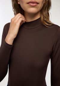 Maglione a maniche lunghe color marrone con collo alto, realizzato in un tessuto morbido e elastico. Il design aderente presenta un collo alto e dettagli di cucitura sottili.