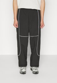 Mustat housut valkoisella reunuksella, joustavalla vyötäröllä, leveillä lahkeilla ja sileällä, kevyellä kankaalla. Yhdistetty harmaisiin ja mustiin kenkiin.