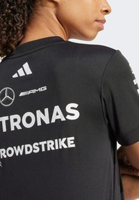 Crna sportska majica s bijelim logotipima PETRONAS, AMG i CROWDSTRIKE. Kratki rukavi, okrugli izrez, izrađena od laganog materijala.
