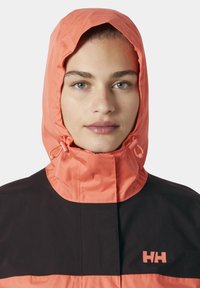 Kapturowa wodoodporna kurtka z koralowym kapturem i czarnym korpusem, z detalem sznurka i logo na klatce piersiowej. Gładka faktura.