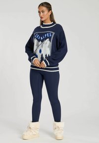 Maglione blu navy con grafica di montagna, scollo rotondo e polsini a costine. Abbinato a leggings blu navy e stivali foderati in pelliccia color crema.
