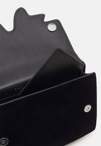 Czarna skórzana kopertówka o fakturowanym wykończeniu, z gładką wewnętrzną kieszenią i srebrnymi detalami. Zaprojektowana z charakterystycznym falistym brzegiem.