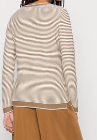 Maglione a maniche lunghe beige e bianco a righe con scollo rotondo e texture a costine, completato da un orlo e polsini a contrasto.