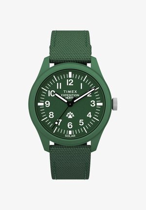 Zeleni Timex Expedition solarni sat s teksturiranim tekstilnim remenom, zaobljenim plastičnim kućištem, bijelim i crnim oznakama sati, te grafikom planine na brojčaniku.
