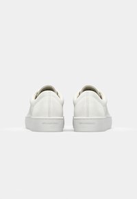 Baskets en cuir blanc avec une forme arrondie, des semelles en caoutchouc plates et un design minimaliste. L'arrière présente des coutures discrètes et un logo.