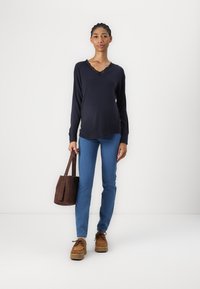 Chemise à manches longues marine avec un col en dentelle, jeans moulants bleus, chaussures à plateforme brunes et un petit sac à main brun. Texture lisse sur l'ensemble.