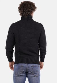 Maglione nero lavorato a maglia con colletto alto, polsini e orlo a coste. Motivo testurizzato con silhouette aderente. Indossato con jeans blu.