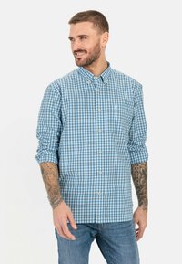 Blauwe en witte gingham ruitjes blouse met lange mouwen, een opgestikte zak en een knoopkraag; gemaakt van zacht katoen.
