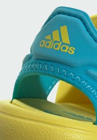 Sandali Adidas con una toma turchese e dettagli di cucitura, accenti gialli sulla soletta e una suola gialla testurizzata.