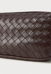 Clutch de pele tecida castanha com uma superfície texturizada e uma borda suave e arredondada. Apresenta um padrão cruzado por toda a parte.
