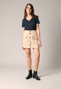 T-shirt bleu marine en col V associé à une mini-jupe en suède beige avec poches avant et boutons noirs, portée avec des bottines noires.