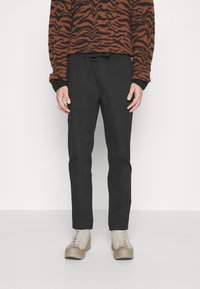 Black stretch trousers with a relaxed fit, elastic waistband, and side pockets, paired with light-colored boots and a patterned sweater.