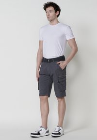 Grijze cargobermuda's voor mannen met meerdere zakken en een riem, gemaakt van lichtgewicht stof, gecombineerd met een effen wit T-shirt en zwart-witte sneakers.